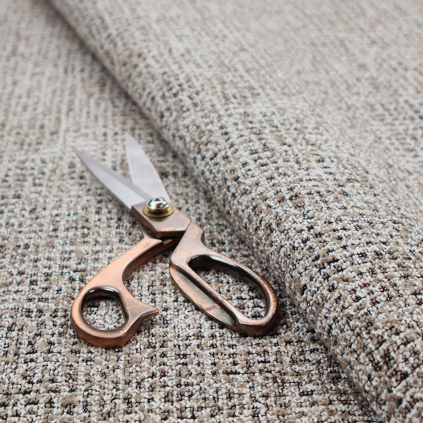 A textured, woven fabric featuring a complex pattern of beige, black, and white threads, creating a speckled and mottled appearance.