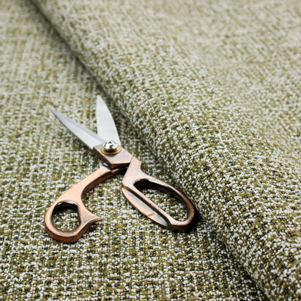A textured, woven fabric featuring a complex pattern of green, dark, and white threads, creating a speckled and mottled appearance.