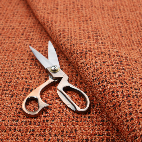 A textured, woven fabric featuring a complex pattern of orange, dark, and beige threads, creating a speckled and mottled appearance.