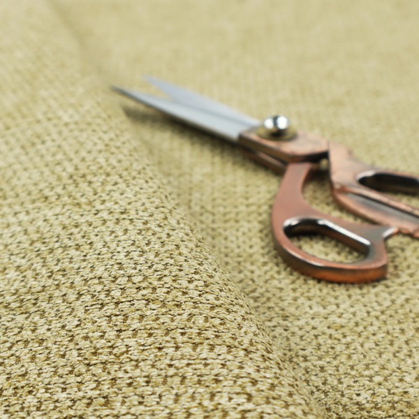 A textured fabric in a warm olive or golden-khaki tone. The material features a tight, rhythmic weave with a prominent tactile surface. The colour is a rich, earthy sage, achieved by interlacing olive-green threads with lighter tan and straw-coloured fibres, creating a weathered, organic look that shifts beautifully in the light.