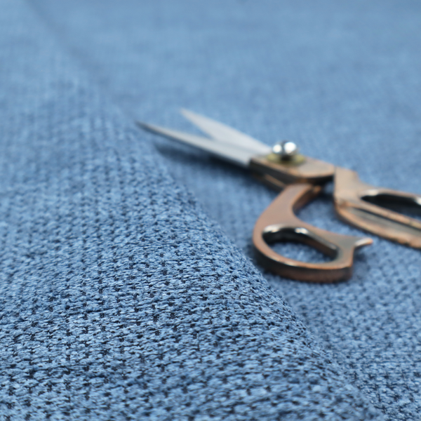 A textured fabric in a serene slate or denim blue tone. This material features a dense, rhythmic weave with a tactile, honeycomb-like surface. The colour is a cool, mid-toned blue, achieved by interlacing cornflower blue threads with darker charcoal base fibres, resulting in a weathered, multidimensional look that feels both calm and sturdy.