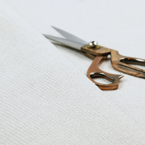 A light-coloured, woven contract fabric. The material features a fine, grid-like texture resembling a mix of linen and grass cloth in a neutral off-white or pale pearl tone. The weave creates a subtle, matte geometric pattern with delicate shadows that give the surface a tactile, three-dimensional appearance.