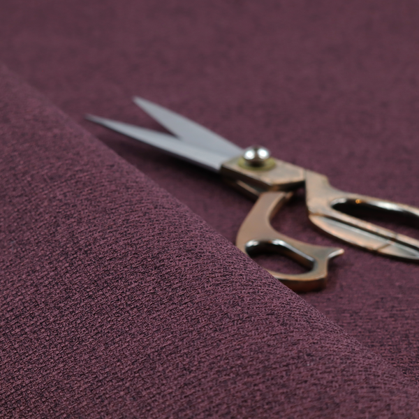 an upholstery fabric in a rich plum or deep burgundy shade. The textile features a dense, multi-tonal weave with interlacing threads of dark purple, berry, and charcoal, creating a textured, linen-look surface with a sophisticated matte finish.
