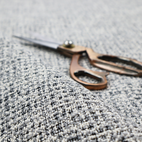 A dense, multi-tonal grey woven fabric. The textile features a salt-and-pepper blend of charcoal, silver-grey, and off-white yarns in a tactile, nubby bouclé weave.