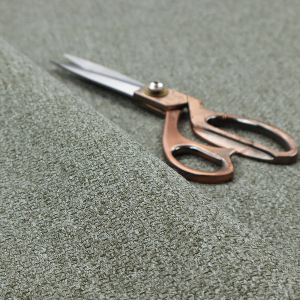 A textured woven upholstery fabric. The material features a dense, multi-tonal weave of sage green, grey, and beige threads, creating a speckled effect with a tactile, matte finish.