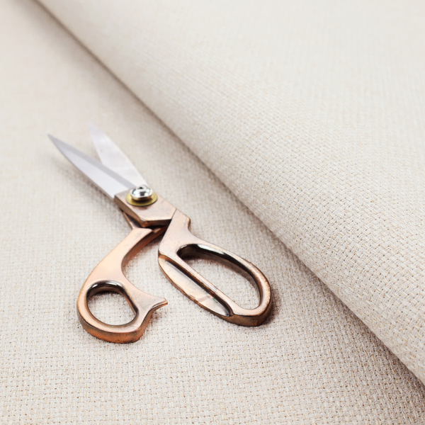 A cream or off-white fabric featuring a distinct, tightly woven grid texture. The material has a uniform, basket-weave style pattern with subtle variations in tone, creating a soft, warm, and matte finish across the entire surface.