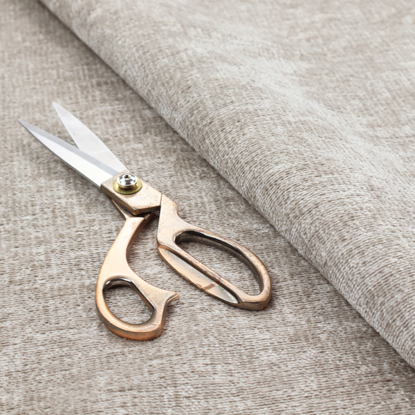 A textured fabric swatch in a light, neutral taupe or sandy beige colour. The material features a dense, uniform nubby weave with subtle horizontal striations and warm grey undertones, creating a soft, multi-tonal appearance.
