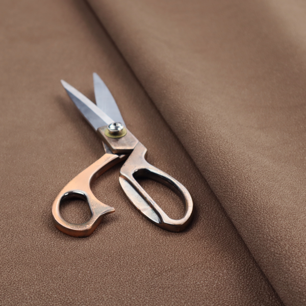 A dark brown or chestnut Merida Suede upholstery fabric. The textile features a highly detailed, dense, and uniform embossed pebbled pattern, giving the soft suede material an intricate, tactile shagreen texture.