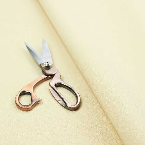A light cream or soft ivory Merida Suede upholstery fabric. The textile features a highly detailed, dense, and uniform embossed pebbled pattern, giving the soft suede material an intricate, tactile shagreen texture.