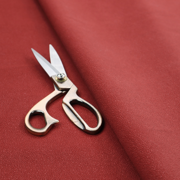 A rich crimson or deep red Merida Suede upholstery fabric. The textile features a highly detailed, dense, and uniform embossed pebbled pattern, giving the soft suede material an intricate, tactile shagreen texture.