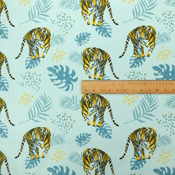 A tropical jungle upholstery fabric on a light mint-blue background featuring a repeating pattern of yellow and black tigers surrounded by teal monstera leaves, palm fronds, and yellow dot clusters.