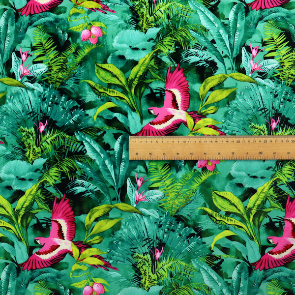 Tropical fabric featuring vibrant magenta parrots in flight surrounded by lush green palm fronds, banana leaves, and pink tropical flowers.