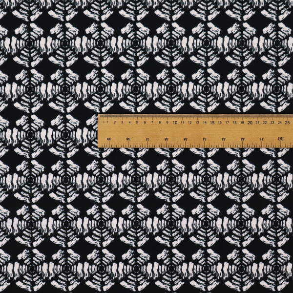 A bold, monochrome fabric pattern featuring a repeating hand-inked radial geometric design in cream on a solid black background.