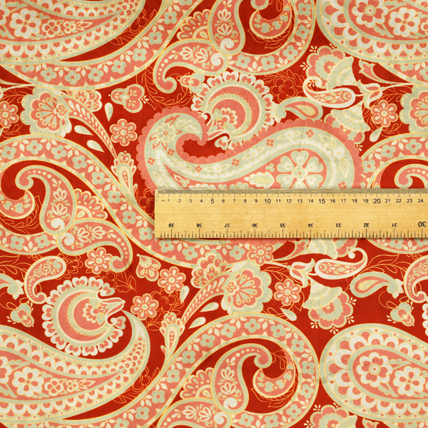 A vibrant, warm-toned textile featuring large-scale paisley teardrop motifs in shades of cream, pale mint, and soft orange against a bold red background. The intricate patterns within the paisley shapes include delicate floral borders and internal mandalas, surrounded by smaller scattered flower accents for a rich, traditional Indian-inspired aesthetic.