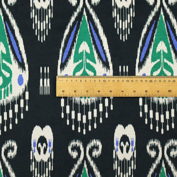 A dark textile featuring rows of floating, feathered ikat medallions. The design glows with emerald green and bright sapphire blue against a deep obsidian background, accented by crisp white geometric tassels and swirling crown-like scrollwork.