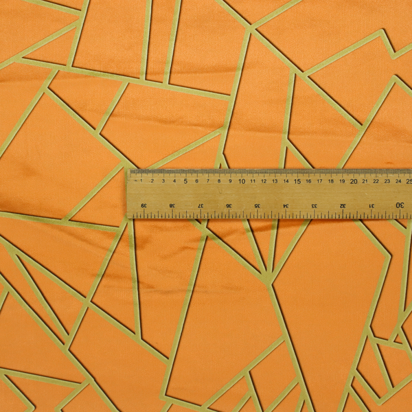 A close-up of a luxurious bright orange or apricot fabric featuring a fractured, geometric mosaic pattern. The warm, vibrant background is segmented by a network of recessed metallic gold lines that form sharp, irregular polygons. This "shattered-glass" effect pairs a bold, citrus-toned base with shimmering, Art Deco-inspired gold linework, creating a high-contrast and architectural look with a subtle 3D texture.
