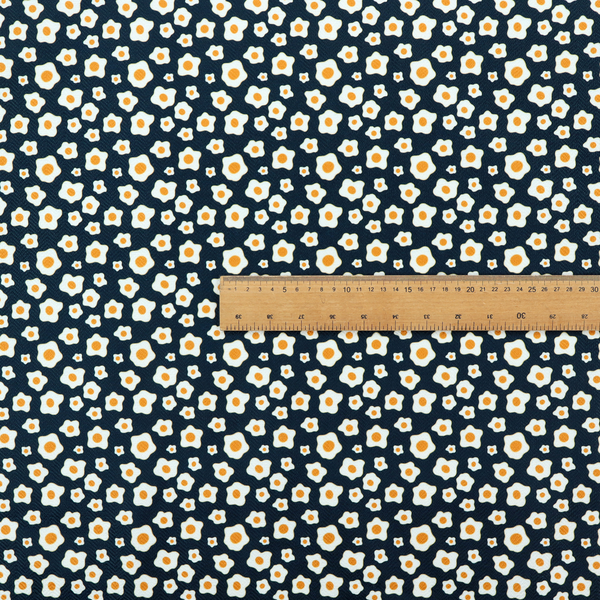 A dark navy blue fabric featuring a dense, repeating pattern of small fried egg motifs with white whites and yellow yolks.