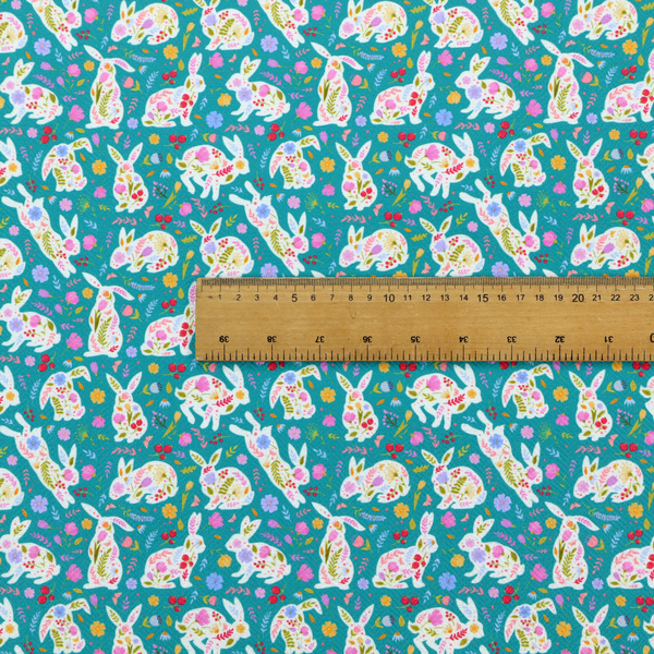 This fabric features a vibrant, folk-art inspired Easter pattern set against a rich teal-green background. The design is characterized by its high-contrast colour palette and intricate floral silhouettes.