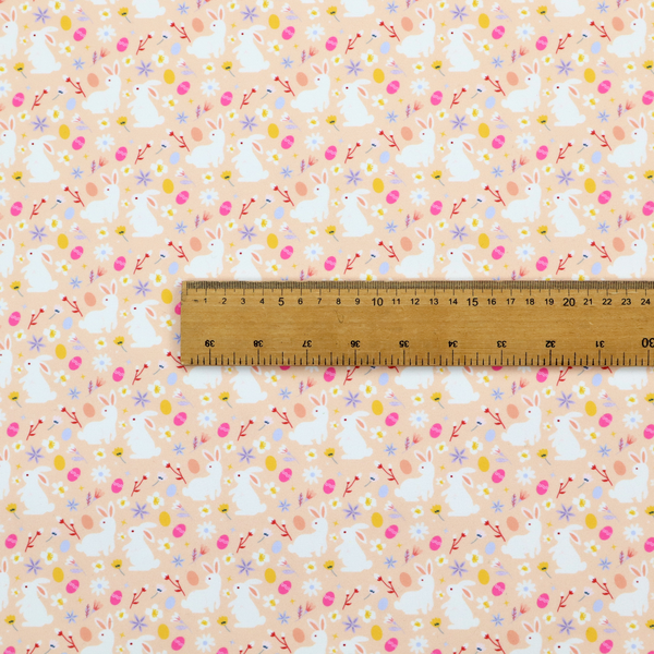 This fabric features a delicate, dainty Easter meadow pattern on a soft, peachy-beige background. The design is airy and feminine, characterized by small-scale illustrations and a palette of pastel and vibrant spring colours.