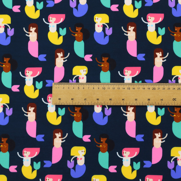 A fun and vibrant children's fabric on a deep midnight-navy background. The pattern features a diverse cast of illustrated mermaids with various skin tones, hair colours (pink, blonde, brown), and colourful tails in shades of mint, yellow, pink, and purple, arranged in a cheerful repeating grid.