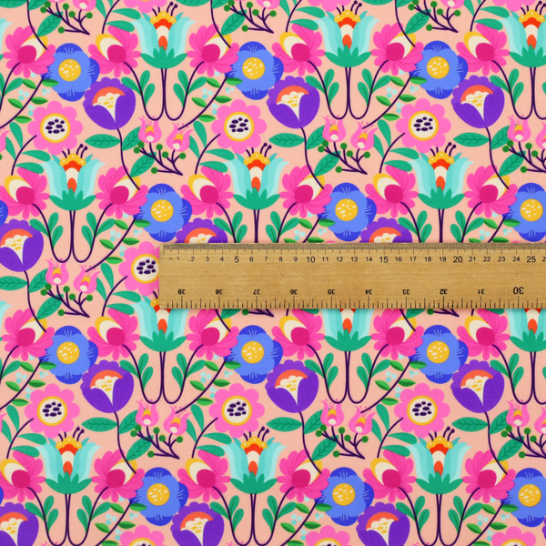 A vibrant and energetic floral fabric on a soft peach-blush background. The design features a symmetrical folk-art arrangement of stylized flowers in neon pink, electric blue, violet, and turquoise, connected by emerald green leaves and delicate black stems in a dense, mirrored repeat.