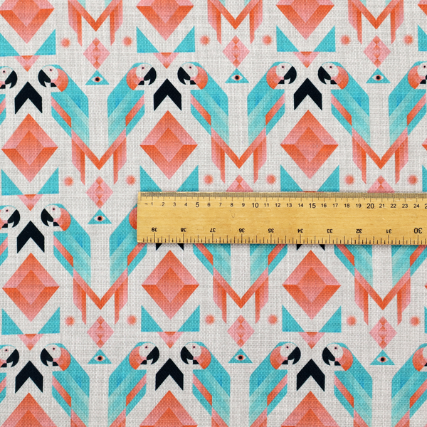 A modern and vibrant geometric fabric on a textured, off-white linen-look background. The design features a symmetrical repeat of abstract parrots rendered in sharp, angular 'prism' shapes of turquoise, coral-pink, and charcoal black. Interspersed between the birds are large coral diamonds and teal triangles, creating a balanced, contemporary tribal-pop aesthetic.