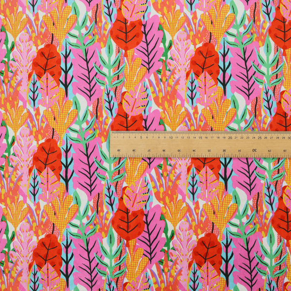 A vibrant, repeating textile pattern featuring a dense arrangement of stylized tropical leaves in saturated shades of pink, orange, yellow, and bright green against a white background.