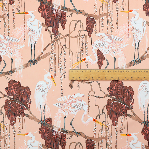 A peach-pink fabric with an illustrated botanical and avian pattern featuring white egrets perched on brown branches among dark red, stylized foliage and weeping floral tendrils.