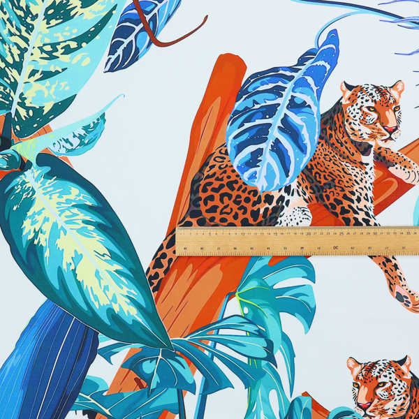 Pattern fabric featuring leopards resting on orange branches amidst vibrant blue and turquoise tropical leaves and foliage against a light background.