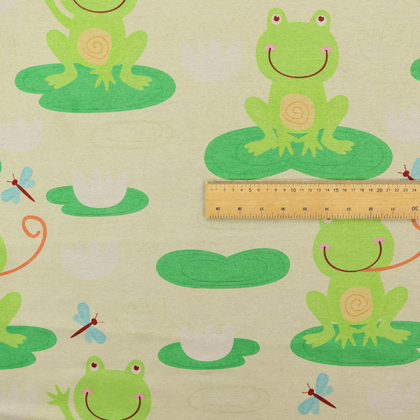 A repeating pattern fabric featuring cute cartoon green frogs sitting on bright green lily pads, interspersed with blue and red dragonflies and white water lilies on a light cream background.