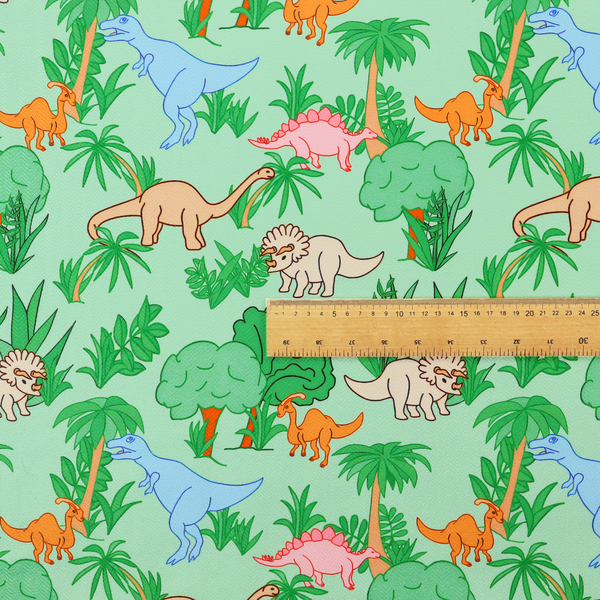 A repeating pattern on a light green background featuring colourful illustrated dinosaurs—including blue T-Rexes, pink Stegosauruses, beige Triceratopses, and orange sauropods—surrounded by green palm trees, bushes, and tropical foliage.