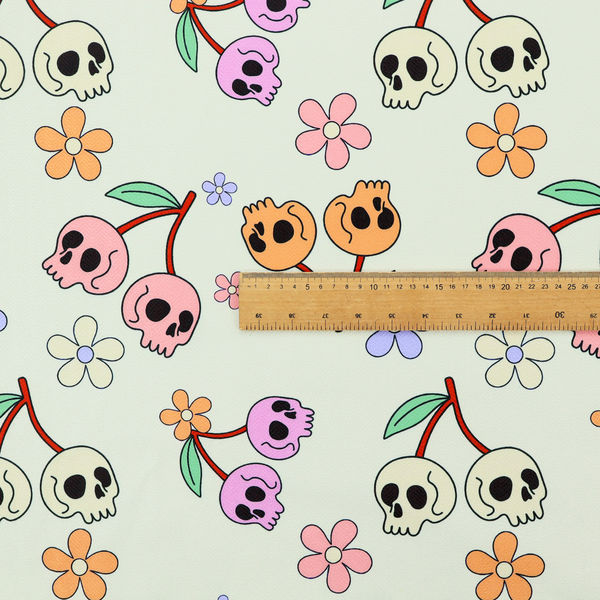 A light retro-style pattern featuring whimsical cherry pairs where the fruit is shaped like colourful skulls in shades of cream, pink, orange, and purple, accented by simple pastel flowers.