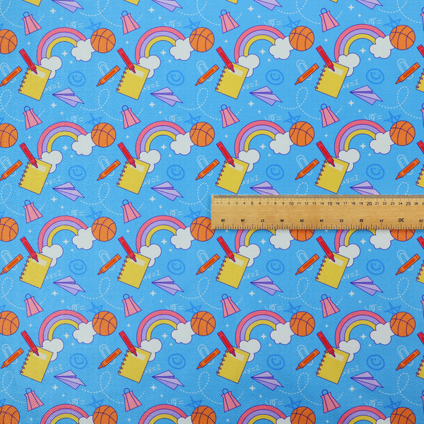 Blue fabric featuring a playful back-to-school pattern with colourful rainbows, basketballs, yellow notebooks with red pencils, purple paper airplanes, and school supplies scattered across a bright blue background.