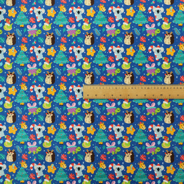 A repeating festive Christmas print on a royal blue background featuring cute cartoon holiday characters, including koalas wearing Santa hats, hedgehogs with antlers, giraffes, Christmas trees, wrapped presents, and stars.