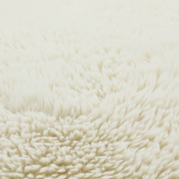 A cream or off-white, high-pile faux fur fabric. The texture appears soft, fluffy, and dense, characterized by long, slightly tousled fibres that give it a cosy, shag-like appearance.