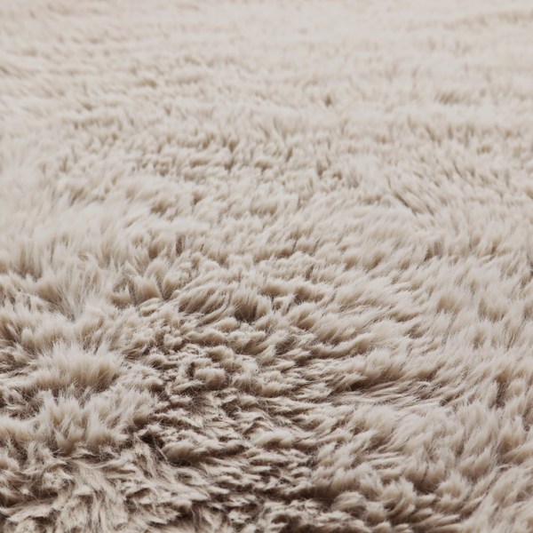 A taupe or light greyish-brown, high-pile faux fur fabric. It features a dense, plush texture with soft, tousled fibres that create a cosy, shag-like appearance.