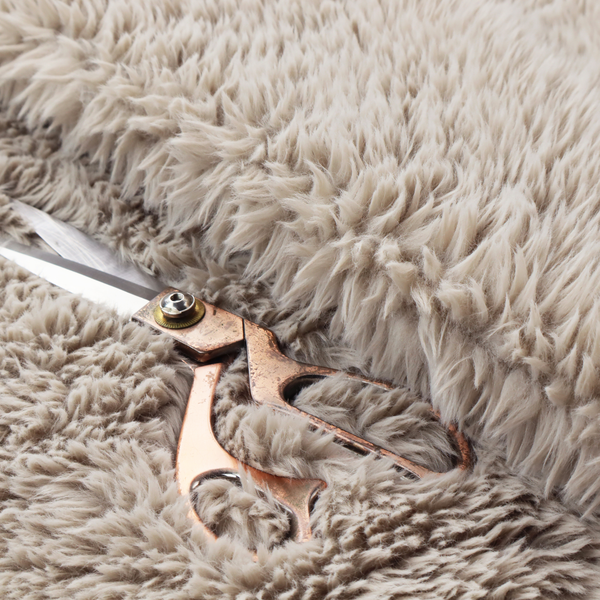 A taupe or light greyish-brown, high-pile faux fur fabric. It features a dense, plush texture with soft, tousled fibres that create a cosy, shag-like appearance.