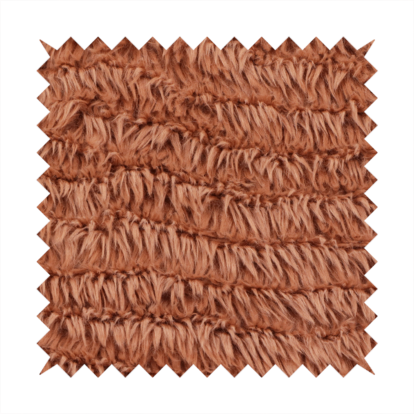 A rust or burnt-orange, high-pile faux fur fabric. It features a unique, wavy or rippled texture created by the directional alignment of the plush, soft fibres, giving it a distinctive shag-like appearance.