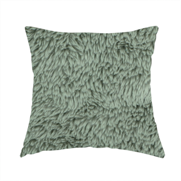 The fabric used to create this handmade cushion is a muted, sage green, high-pile faux fur fabric. It features a dense, luxurious texture with soft, tousled fibres that create a cosy, shag-like appearance.