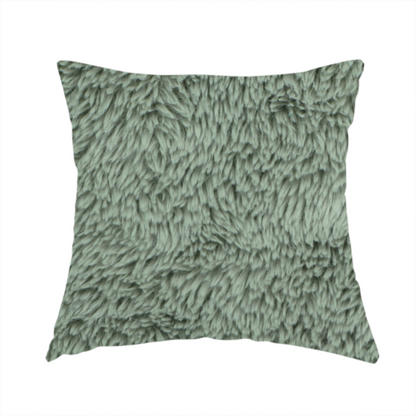 The fabric used to create this handmade cushion is a muted, sage green, high-pile faux fur fabric. It features a dense, luxurious texture with soft, tousled fibres that create a cosy, shag-like appearance.