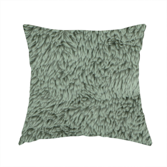 The fabric used to create this handmade cushion is a muted, sage green, high-pile faux fur fabric. It features a dense, luxurious texture with soft, tousled fibres that create a cosy, shag-like appearance.