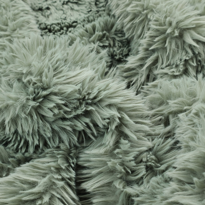 A muted, sage green, high-pile faux fur fabric. It features a dense, luxurious texture with soft, tousled fibres that create a cosy, shag-like appearance.