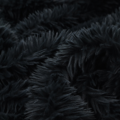 a solid black, high-pile faux fur fabric. It displays a dense, luxurious texture with soft, tousled fibres that create a cosy, sophisticated, and uniform shag-like appearance.