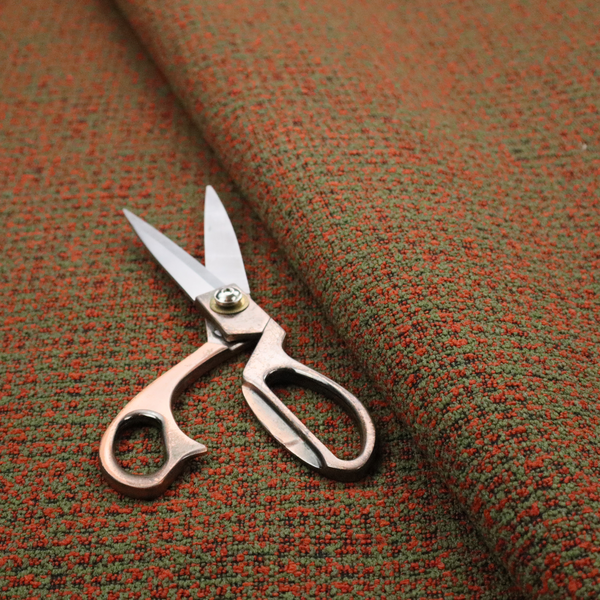 A textured, woven fabric featuring a complex pattern of red, green, and dark threads, creating a speckled and mottled appearance.