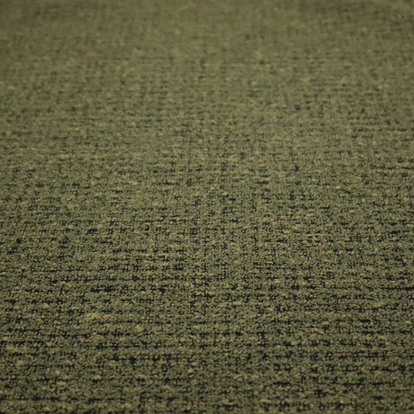 A textured, woven fabric featuring a complex pattern of green, dark, and beige threads, creating a speckled and mottled appearance.