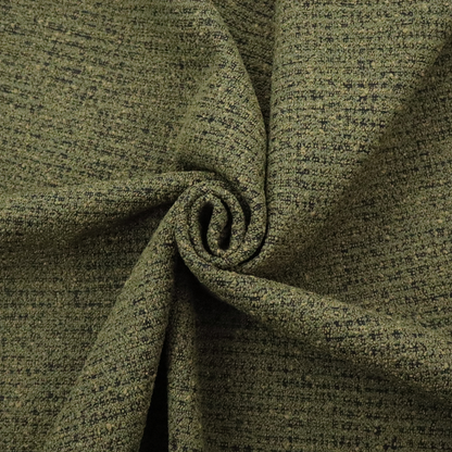 A textured, woven fabric featuring a complex pattern of green, dark, and beige threads, creating a speckled and mottled appearance.