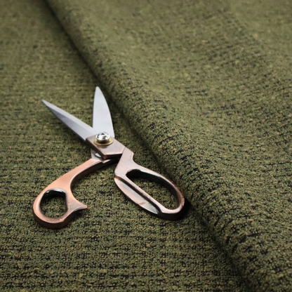 A textured, woven fabric featuring a complex pattern of green, dark, and beige threads, creating a speckled and mottled appearance.