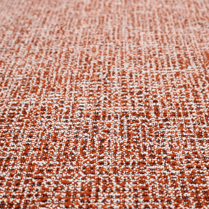 A textured, woven fabric featuring a complex pattern of orange, white, and dark threads, creating a speckled and mottled appearance.