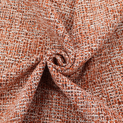 A textured, woven fabric featuring a complex pattern of orange, white, and dark threads, creating a speckled and mottled appearance.