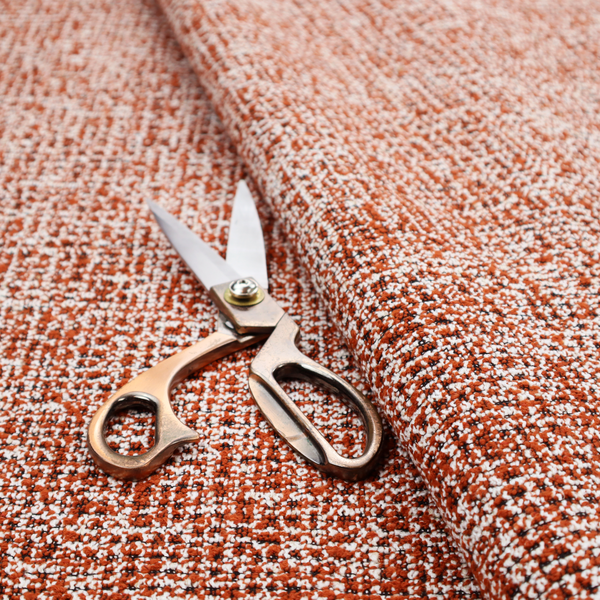 A textured, woven fabric featuring a complex pattern of orange, white, and dark threads, creating a speckled and mottled appearance.